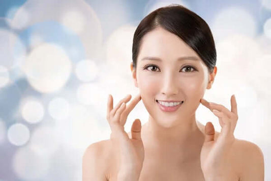 Smiling woman showcasing glowing skin against a soft bokeh background, representing K-beauty principles.