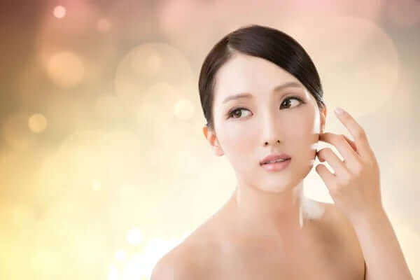 Young woman with flawless skin showcasing Korean beauty routine against a soft bokeh background.