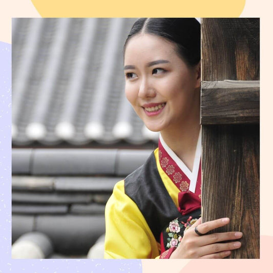 Woman in traditional Korean hanbok smiling while peeking from behind a wooden post.