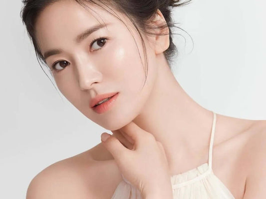 Woman with radiant skin showcasing the glow of Korean glass skin, wearing a light dress and soft makeup.