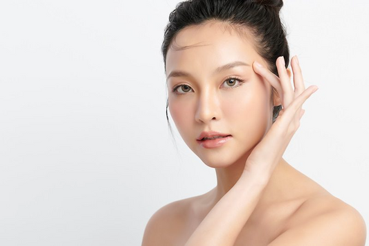 Close-up of a woman showcasing clear, glowing skin while gently touching her face.