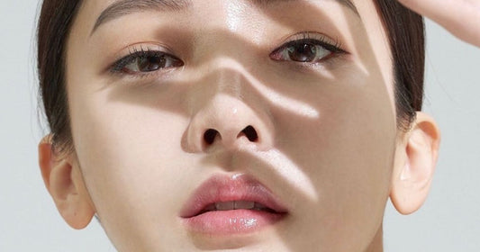 Close-up of a woman's face with radiant skin, illuminated by soft light and shadows highlighting her features.