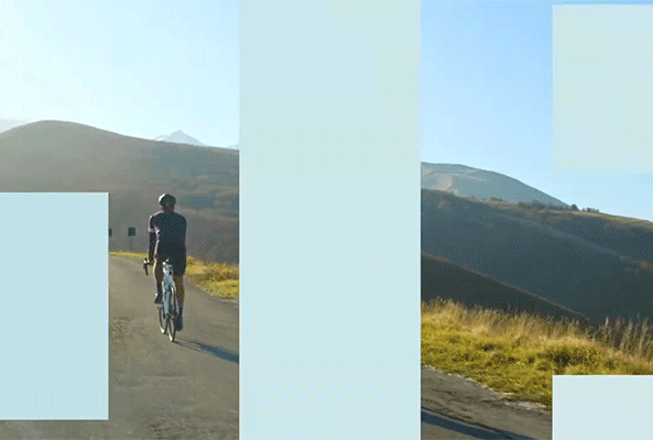 Riman Lifening Nutrition - Cyclist riding along a scenic road with mountains in the background during a sunny day.