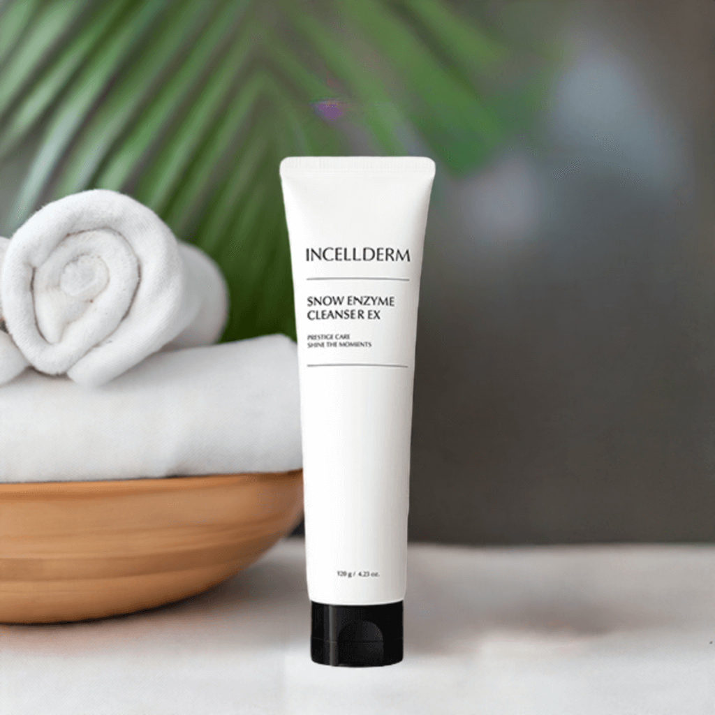 Incellderm Snow Enzyme Cleanser EX tube on a wooden table with rolled towels and tropical greenery in the background.