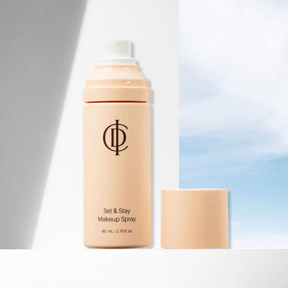 ICD Set & Stay Makeup Spray bottle with cap off against a bright sky backdrop, showcasing skincare-infused makeup setting spray.