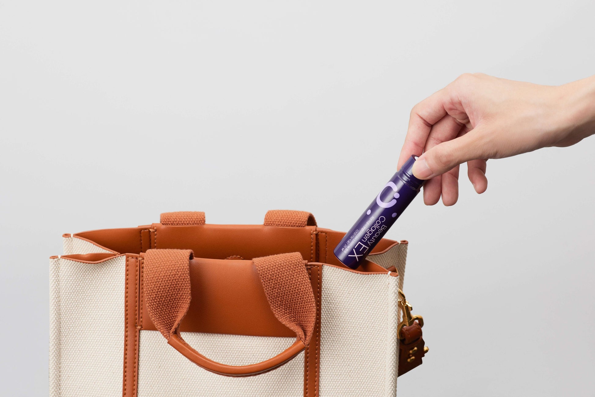 Hand placing Lifening Beauty Collagen EX into beige tote bag, showcasing convenience and portability.
