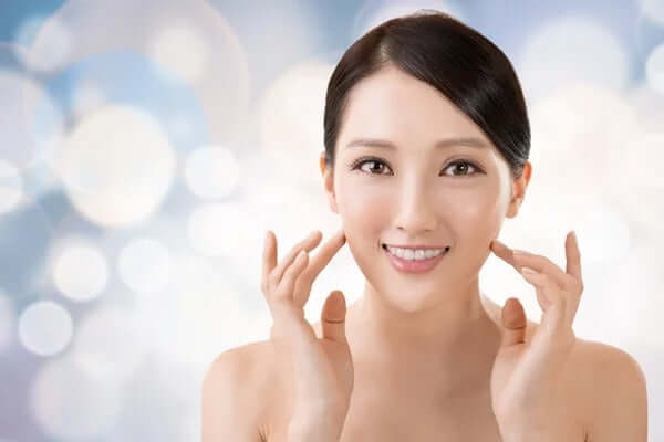 Smiling woman showcasing glowing skin against a soft bokeh background, representing K-beauty principles.