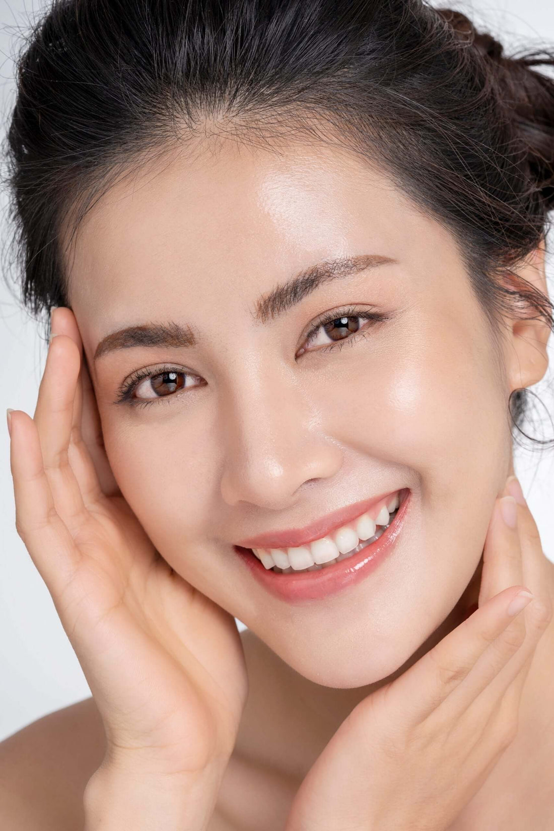 Smiling woman with glowing skin gently touching her face, showcasing a radiant and youthful appearance.