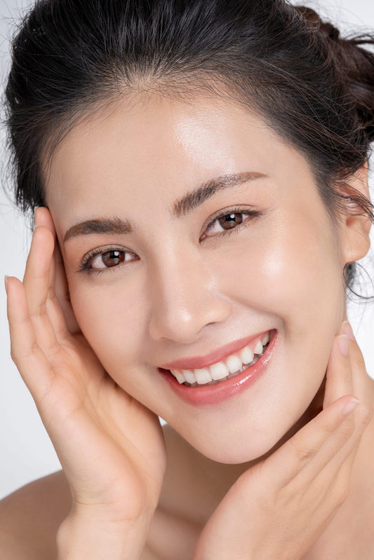 Woman with glowing skin smiling and touching her face, representing healthy skincare routines.